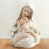 Imagen religiosa de la Madona con el Niño y rosas blancas. Figura devocional de la Virgen María abrazando al Niño Jesús, símbolo de amor maternal y pureza, elaborada en material tipo porcelana blanca con acabado brillante.