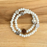 Pulsera rosario elástica doble vuelta en cristal de murano blanco con cruz de madera y medallas de santos en zamak, talla S vista en detalle.