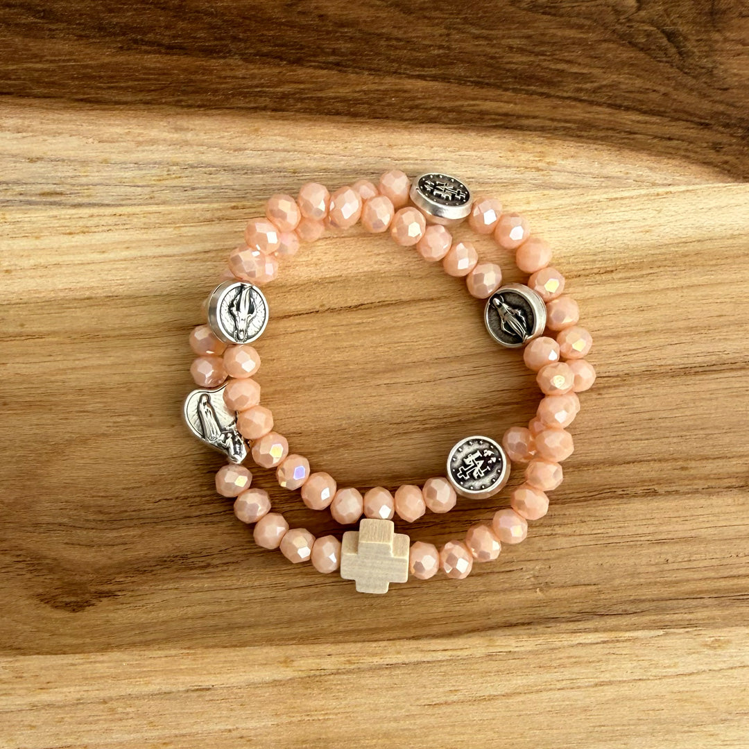 Pulsera rosario elástica en cristal de murano beige talla S con dijes de santos en zamak y cruz de madera vista en detalle
