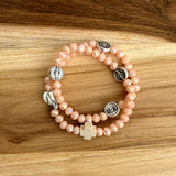 Pulsera rosario elástica en cristal de murano beige talla S con dijes de santos en zamak y cruz de madera vista en detalle