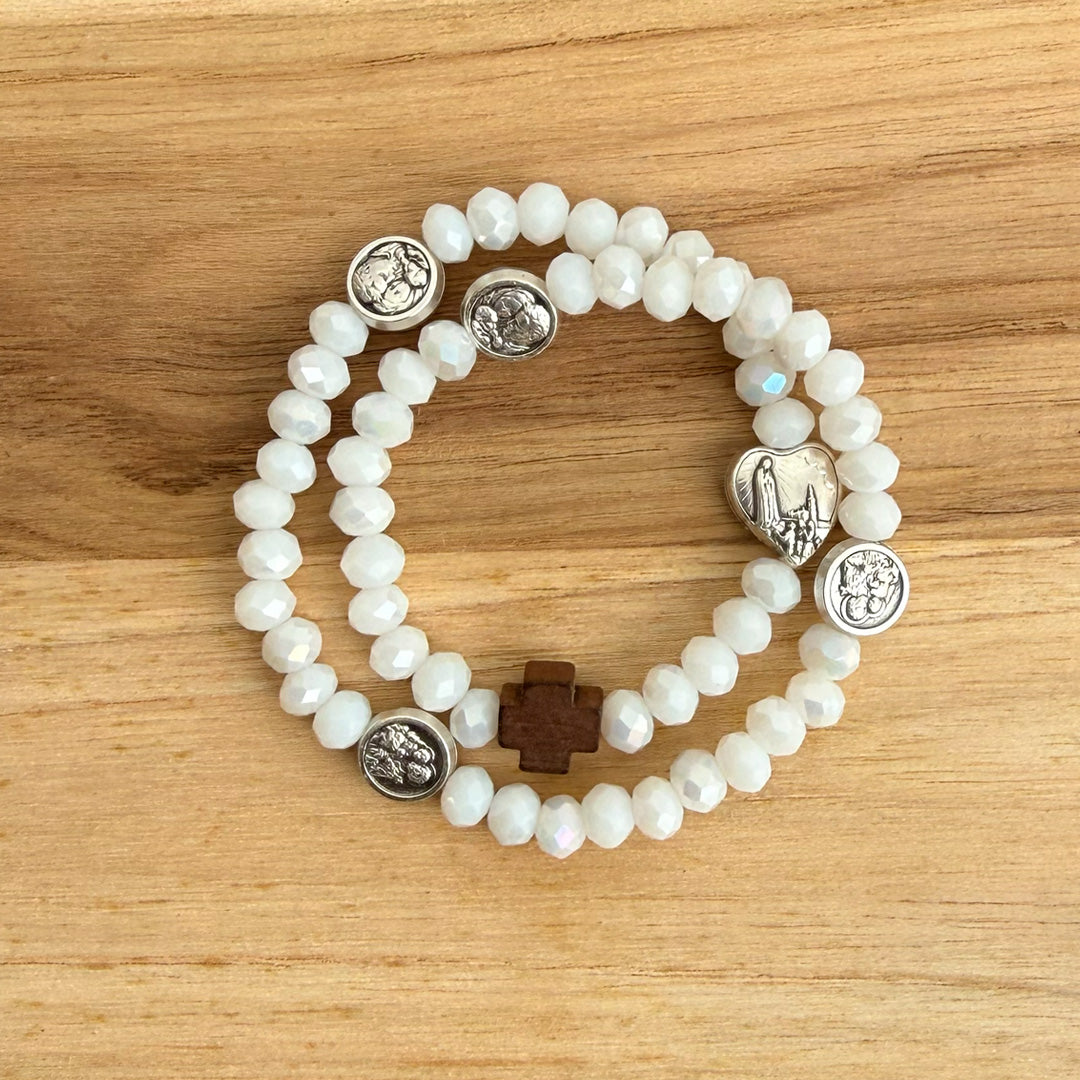 Pulsera rosario elástica doble vuelta en cristal de murano blanco con cruz de madera y medallas de santos en zamak, talla S vista en detalle.