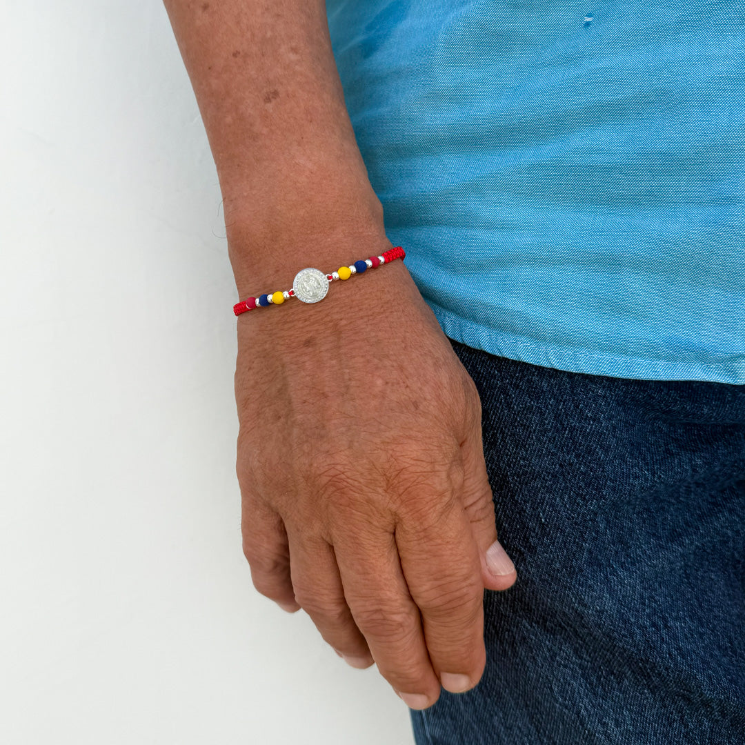 Pulsera de hilo rojo tejido con medalla de plata central y cuentas tricolor de Colombia en neopreno y plata en la muñeca de un hombre.