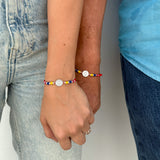 Dos personas tomadas de la mano usando la pulsera tricolor Colombia de hilo rojo con medalla de plata de edición especial.