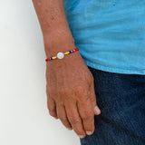 Pulsera de hilo rojo tejido con medalla de plata central y cuentas tricolor de Colombia en neopreno y plata en la muñeca de un hombre.