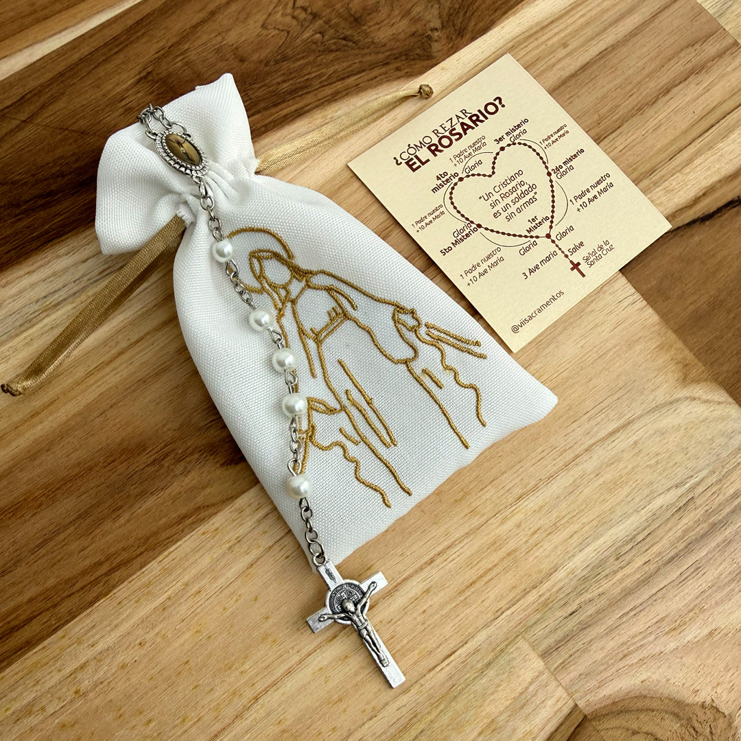 Detalle del rosario de perla de vidrio con cruz de San Benito y tarjeta de misterios sobre fondo de madera.