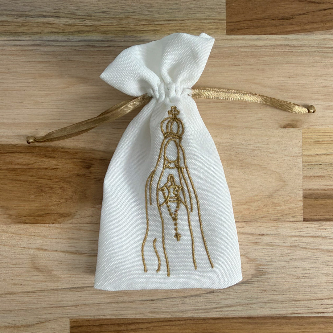 Bolsa de tela blanca bordada en hilo dorado con la silueta de la Virgen de Fátima y lazo de cierre dorado.